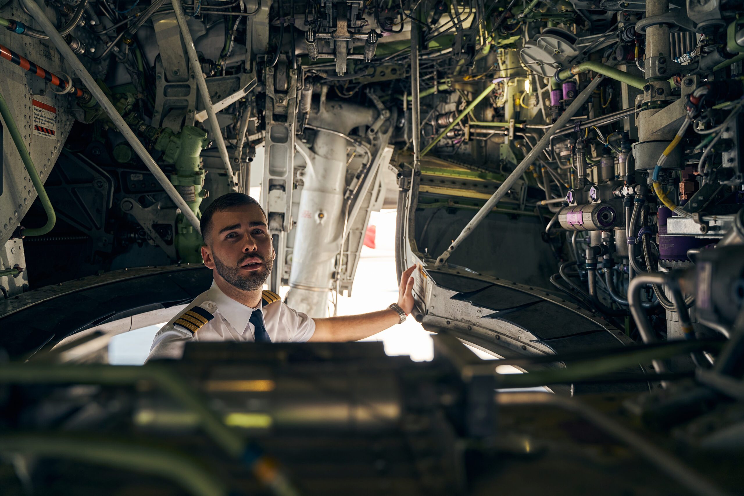 Attractive experienced short-haired bearded man in uniform performing a routine inspection of the airplane bottom