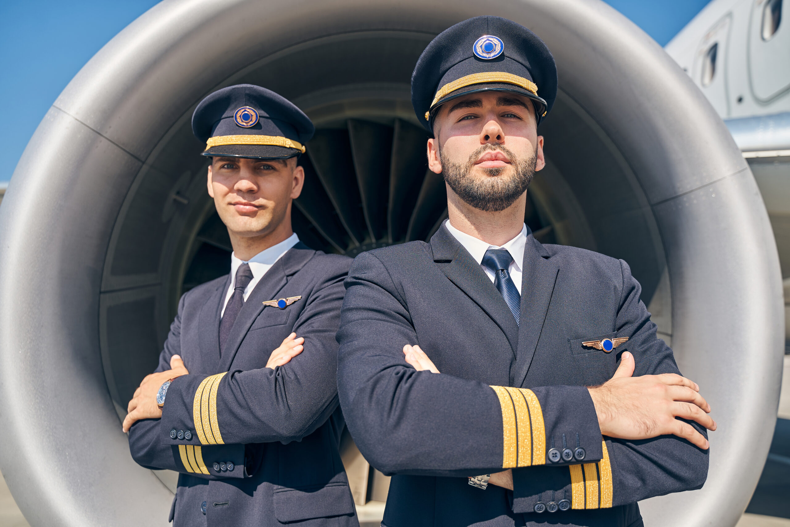 Waist-up portrait of calm young men in uniforms standing in front of the turbofan engine